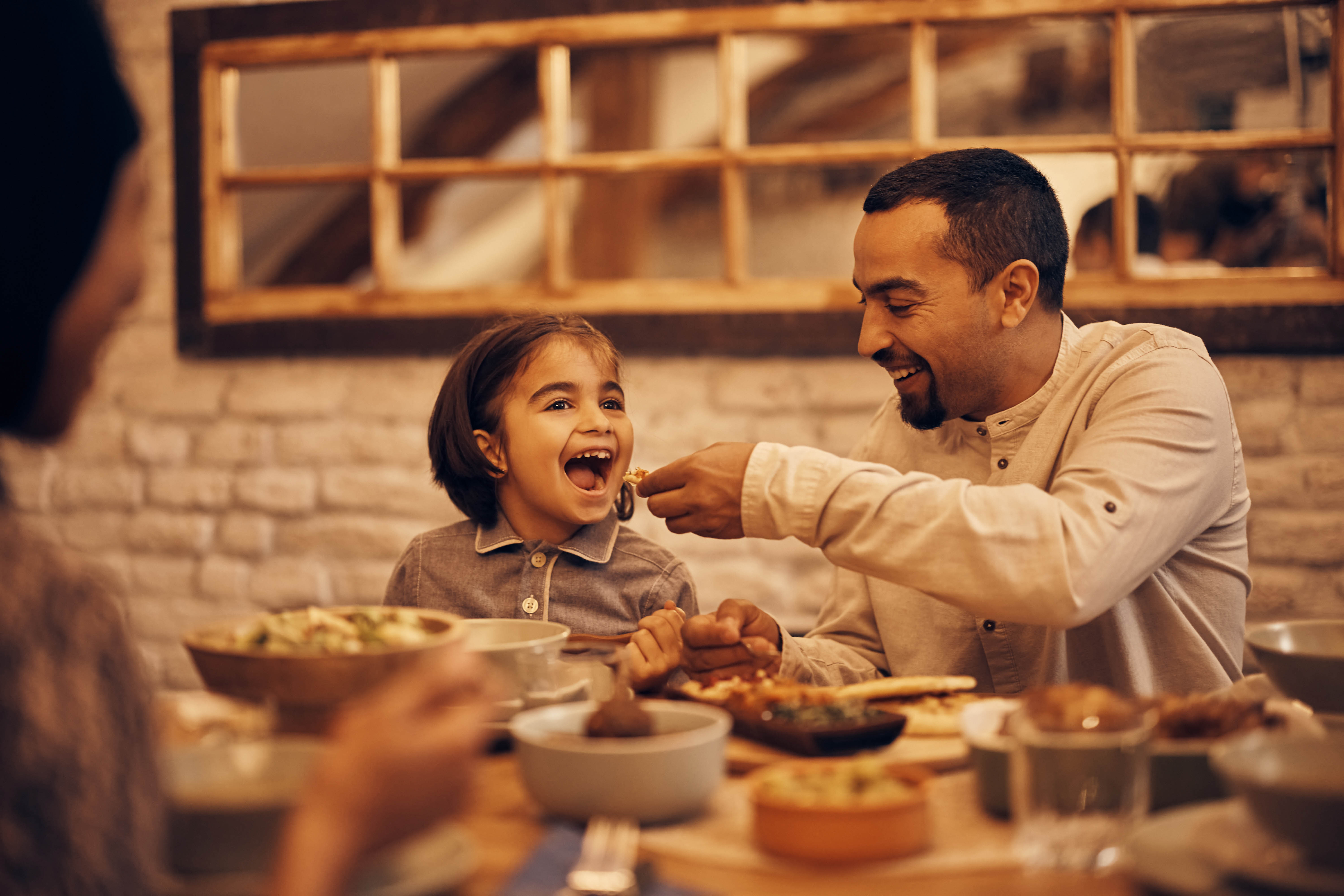 Dad feeding his daughter dinner at the table, picture looking in through the window